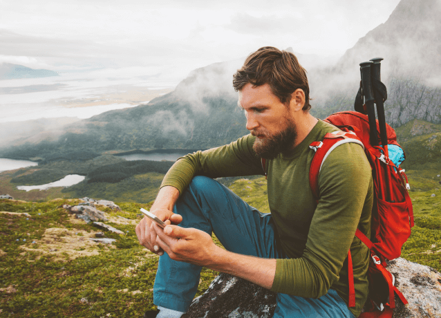 A man sitting on a mountain range using a mobile phone